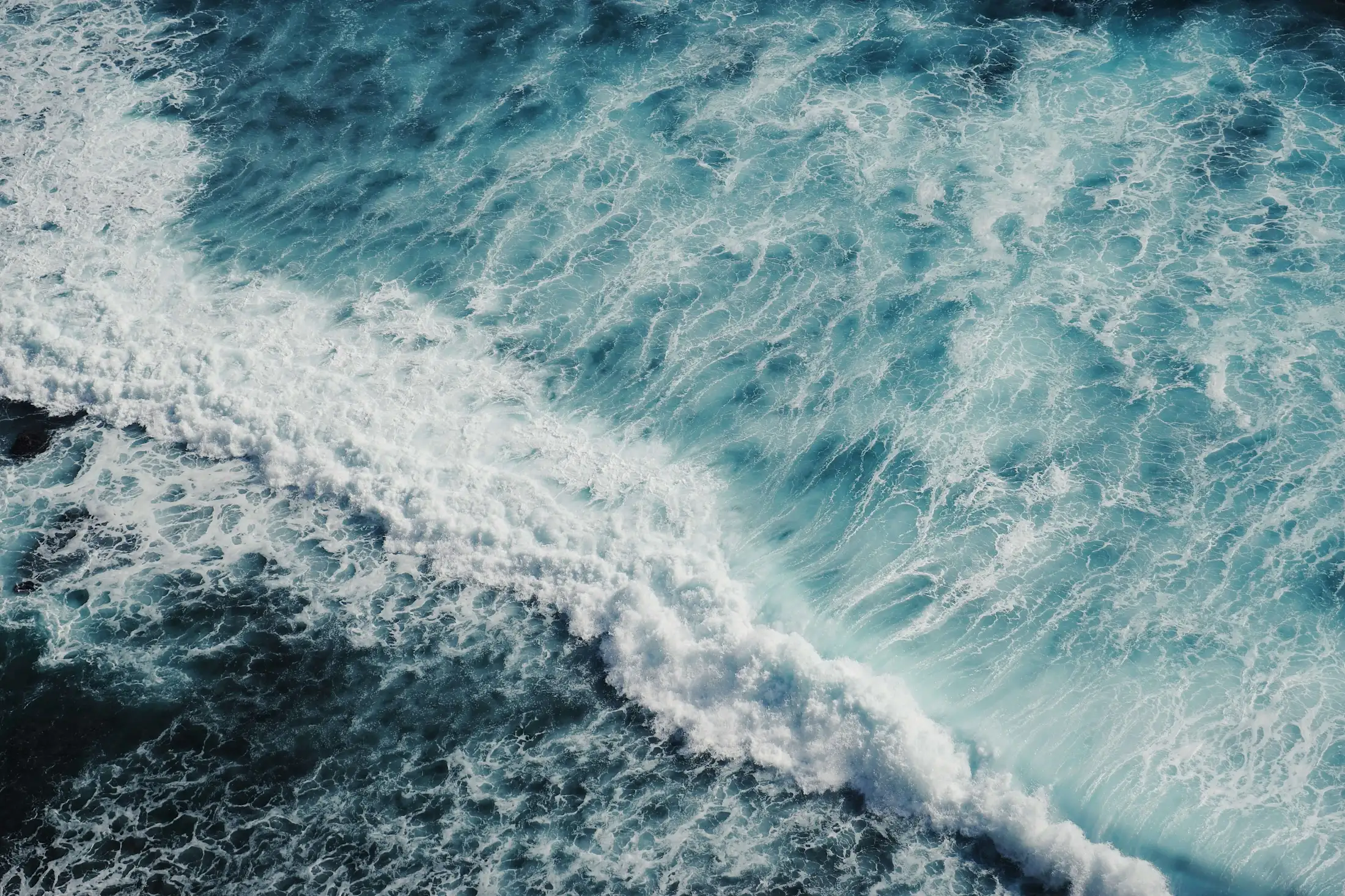 Aerial view of ocean waves crashing and creating white foam on the surface of deep blue water.